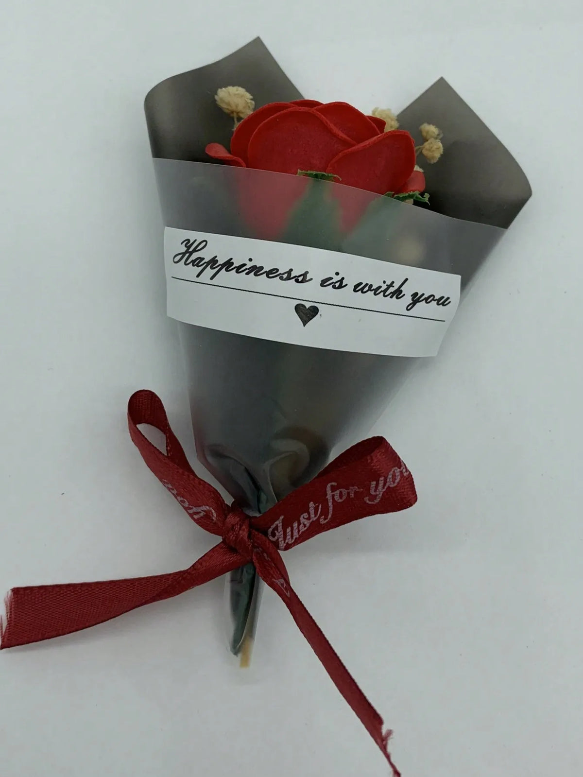 Ein Strauß roter künstlicher Rosen, umwickelt in grauem Papier mit einem Etikett 'Glück ist mit dir' und einer roten Schleife