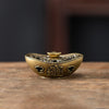 A vintage brass incense burner holder with ornate detailing resting on a wooden surface.