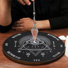 A crystal pendulum hanging from a chain rests on a wooden board used for dowsing and divination.