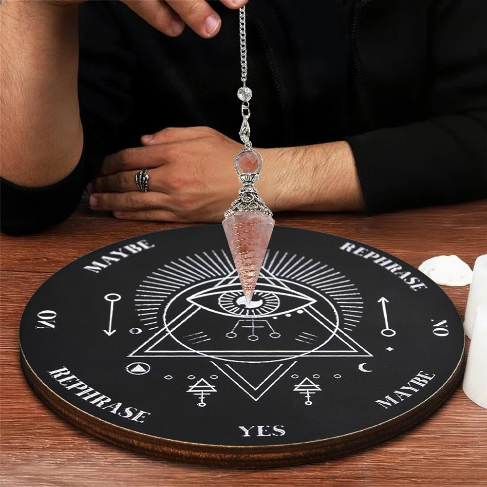 A crystal pendulum hanging from a chain rests on a wooden board used for dowsing and divination.