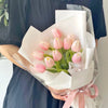 A bouquet of pink tulips wrapped in clear cellophane and white paper, held by a person.