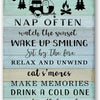 A rustic wooden sign with black text listing camping rules and activities like watching the sunset, sitting by the fire, and 