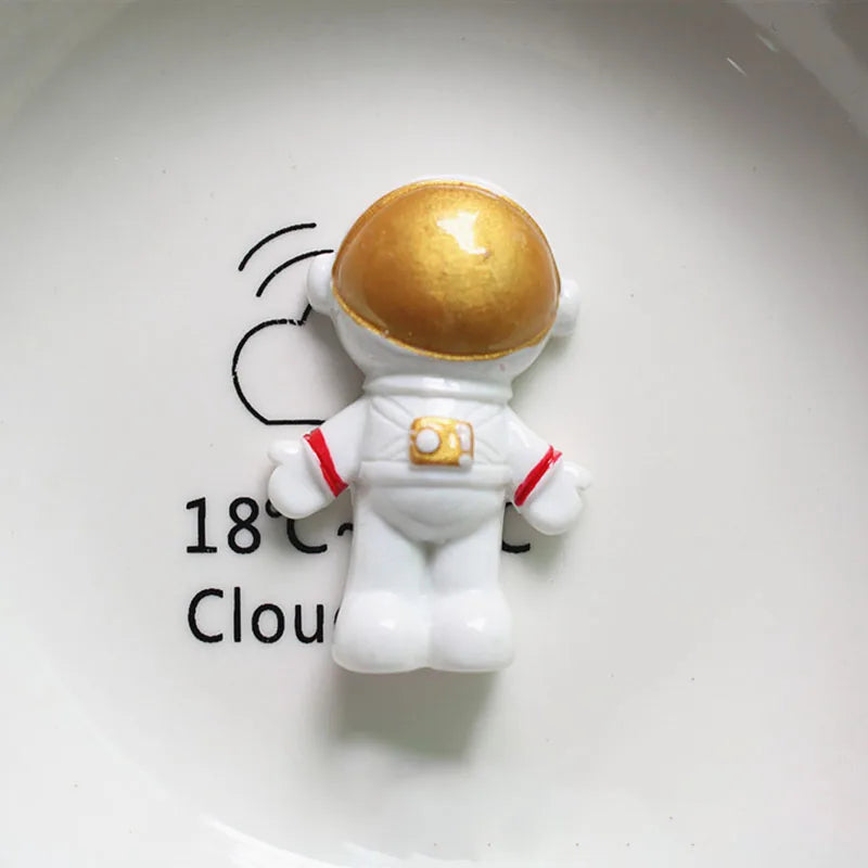 Miniature d'astronaute avec casque doré et combinaison blanche sur une assiette blanche.