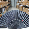A black and white hand folding fan is displayed on a shelf among cardboard boxes.