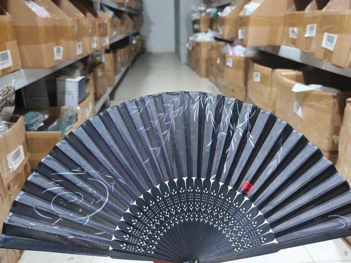 A black and white hand folding fan is displayed on a shelf among cardboard boxes.