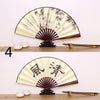 A traditional folding fan with black and cream patterns is displayed on a wooden surface.