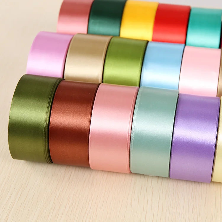 A collection of rolled silk satin ribbons in various pastel and jewel tones arranged in a row.