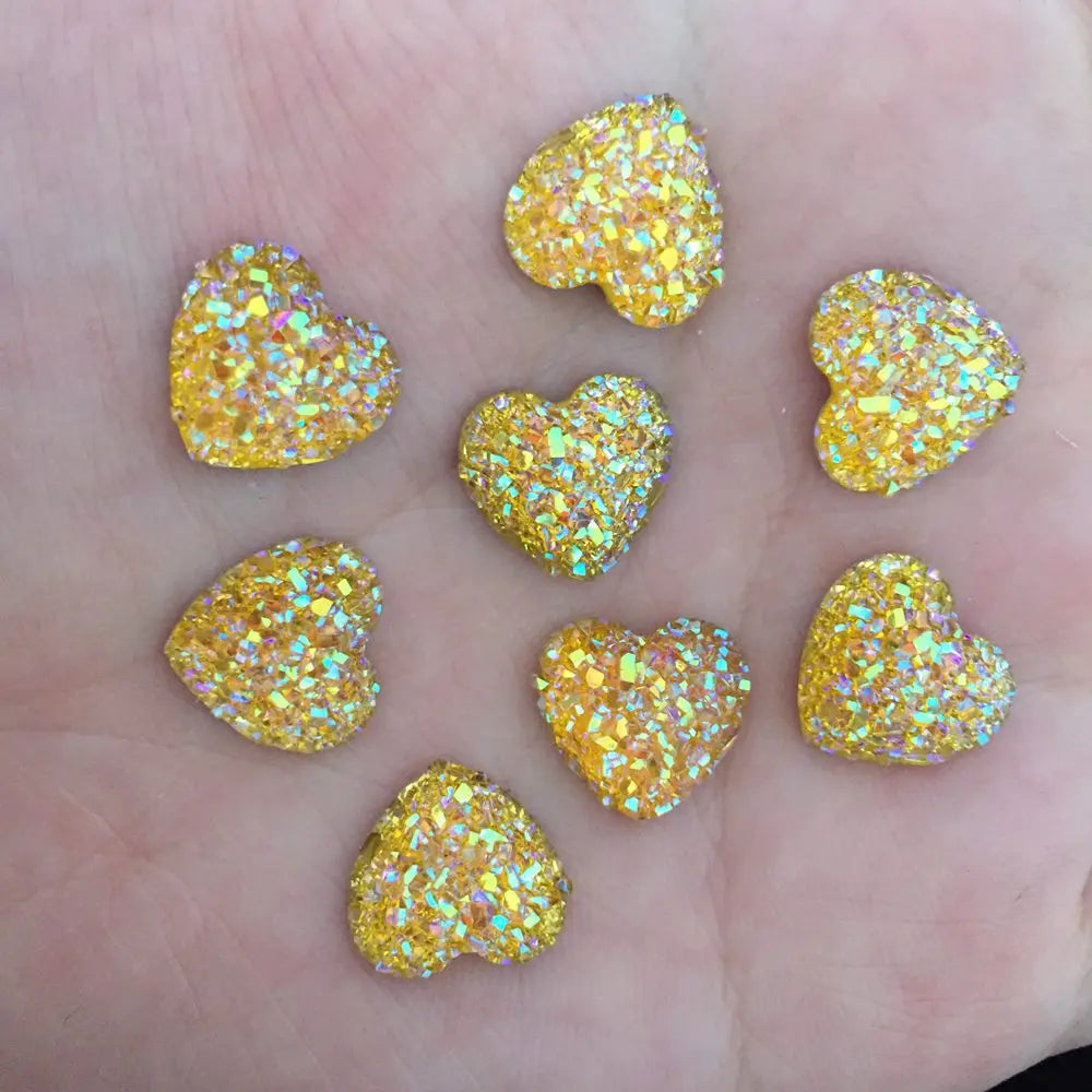 Eine Hand mit kleinen, herzförmigen Dekorationen, bedeckt mit Goldglitzer und Strasssteinen.