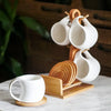 A white ceramic coffee mug set is displayed on a natural bamboo wood stand.