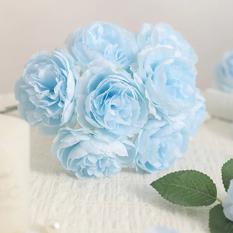 A bouquet of six light blue artificial peony flowers arranged on a white surface.