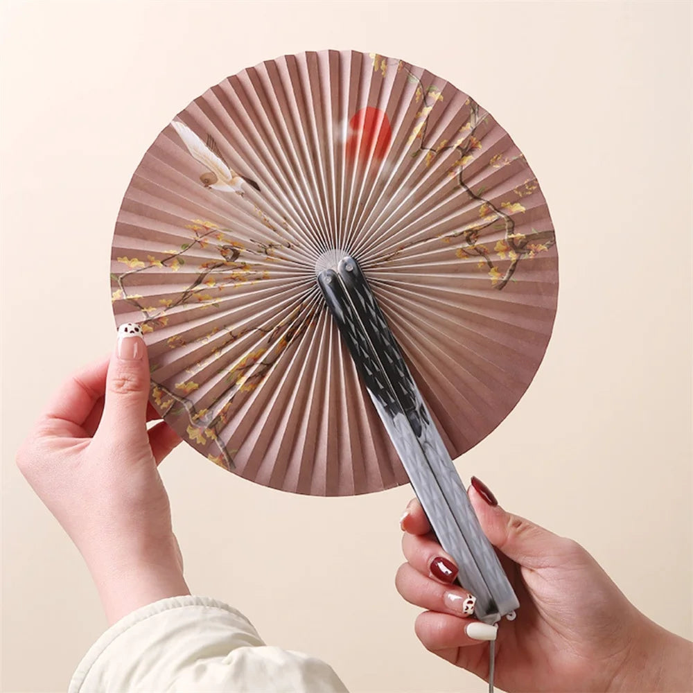 A hand holds a traditional Chinese folding fan with a tassel, showing its pleated surface and dark handle.