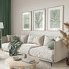 Three framed botanical prints featuring sage green floral designs displayed on a light-colored sofa.