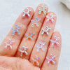 A hand displays various clear and pastel colored balloon puppy nail art charms.