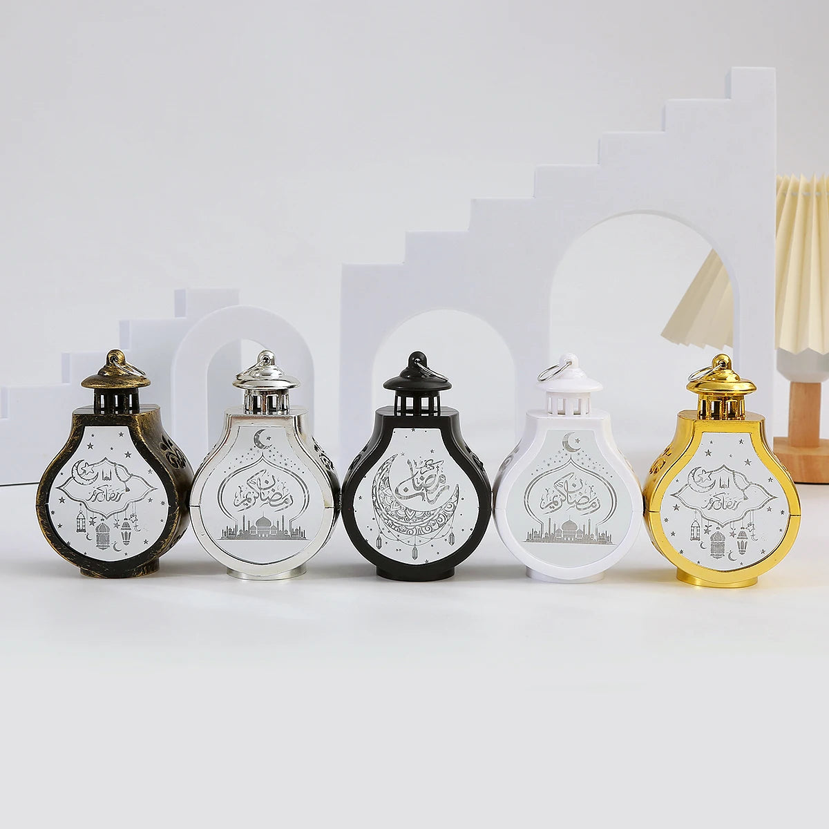 Five decorative lanterns featuring Islamic calligraphy designs in black, white, and gold on a white background.