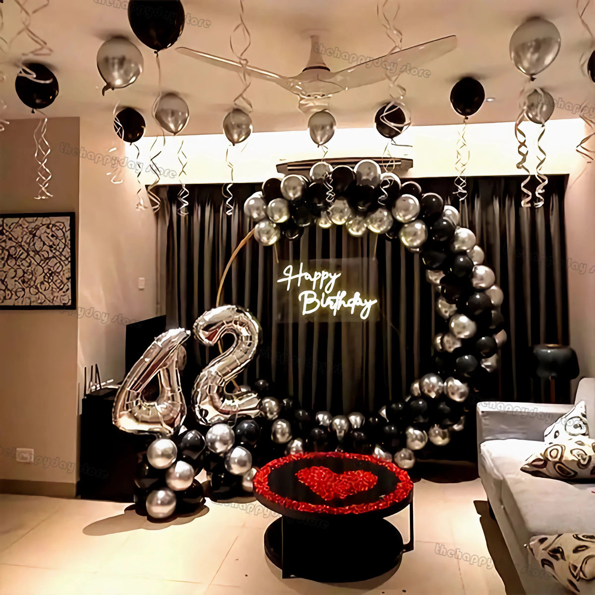 A decorative arch made of silver and black balloons spells out Happy Birthday with a heart design.