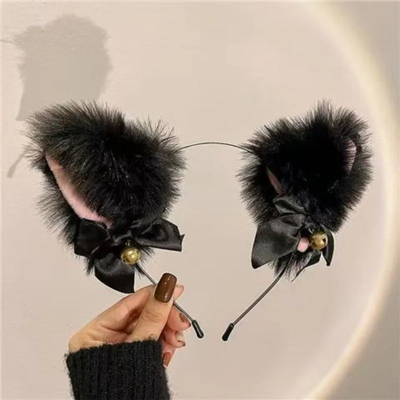 A hand is holding a black faux fur cat ear headband and bell choker set against a light background.
