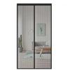 A modern magnetic automatic screen door curtain with vertical slats, featuring a potted plant and wooden furniture visible th