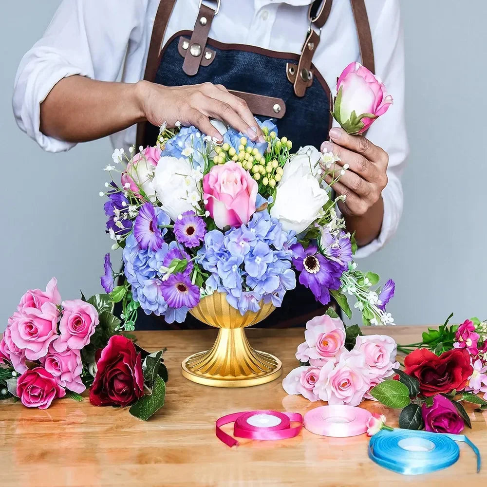 A person holds a bouquet of pink and purple flowers, including roses and hydrangeas, over a wooden table.