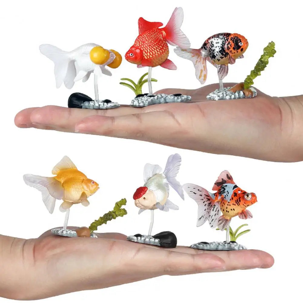 A hand holds several realistic goldfish aquarium decor figurines, including red, orange, and white fish.