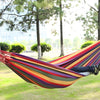 A person lying in a colorful canvas camping hammock suspended between two trees.