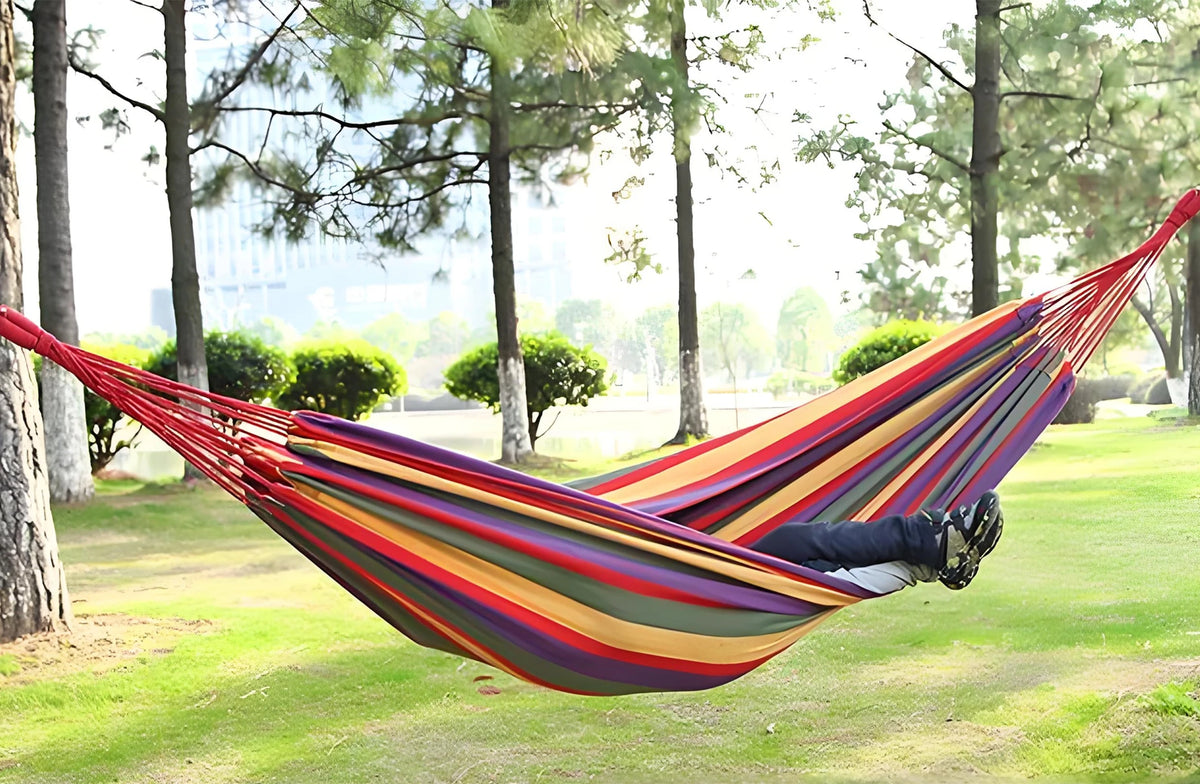 A person lying in a colorful canvas camping hammock suspended between two trees.