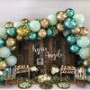A floral arch made of metallic blue and gold latex balloons decorated with greenery and white flowers.