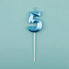 A blue number five candle against a light teal background.