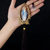 A hand holds a wooden pendant ornament depicting Our Lady of Grace with a blue and white robe.
