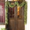 A pair of dark wood doors decorated with a lush green pine vine wreath for holiday decor.