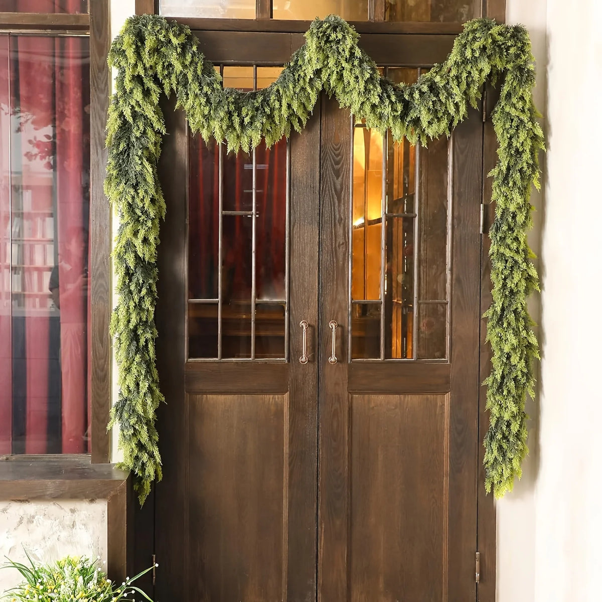 A pair of dark wood doors decorated with a lush green pine vine wreath for holiday decor.