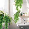 A white ceramic sink area decorated with lush green ivy vines and potted plants.