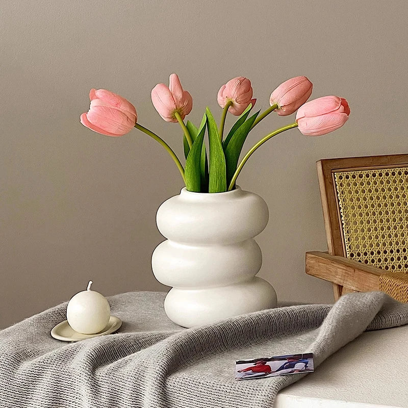 A bouquet of pink tulips in a white ceramic vase on a gray linen cloth.