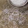 Iridescent nail rhinestones scattered on a surface next to a clear container.