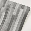 Close-up of realistic wood grain floor stickers showing vertical stripes in shades of gray and white.