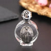 A clear glass bottle containing a religious sculpture of Jesus in an oval frame with a silver cap.
