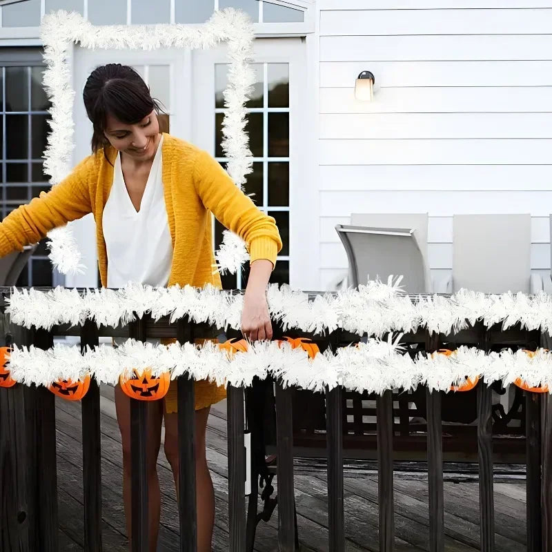 A woman in a yellow sweater is decorating a white picket fence with a tinsel ribbon garland for holiday decor.