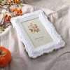 White ornate resin photo frame with a floral embossing displayed on a beige linen fabric.
