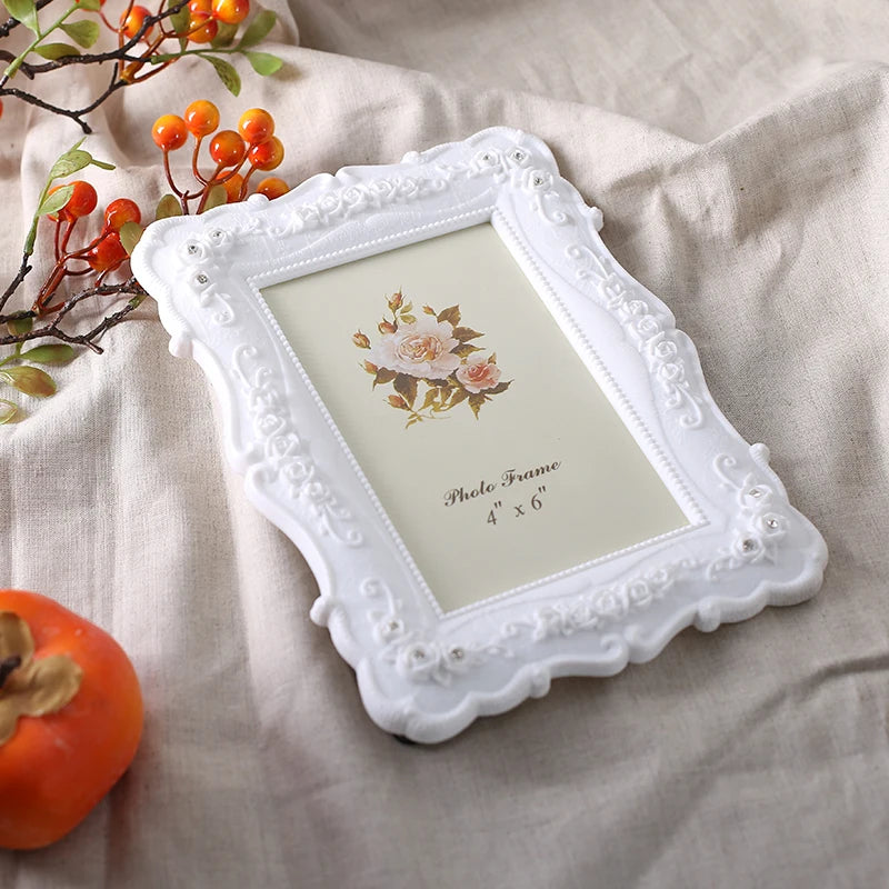 White ornate resin photo frame with a floral embossing displayed on a beige linen fabric.