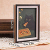A framed print featuring a black cat and a slice of pizza on a dark green background.