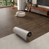 Roll of 3D textured wood grain self-adhesive flooring film placed on a light gray floor.