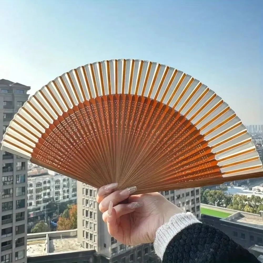 A hand holds an elegant bamboo folding fan with a classic design against a city skyline backdrop.