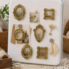 A white tray holds a set of vintage gold-framed resin mini photo frames and natural elements for crafting.