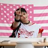 A person holds up a pink American flag tapestry featuring stars and stripes against a white background.