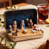A tin containing a nativity scene figurine set featuring figures, sheep, and straw in a gold-colored storage box.