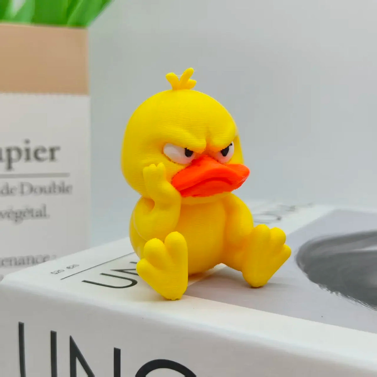 A yellow 3D printed figurine of an angry duck with orange beak and glaring eyes.