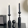 A set of two black decorative candlesticks with lit candles on a dark surface.
