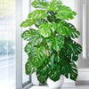 A vibrant artificial monstera plant with large green silk leaves displayed indoors near a window.