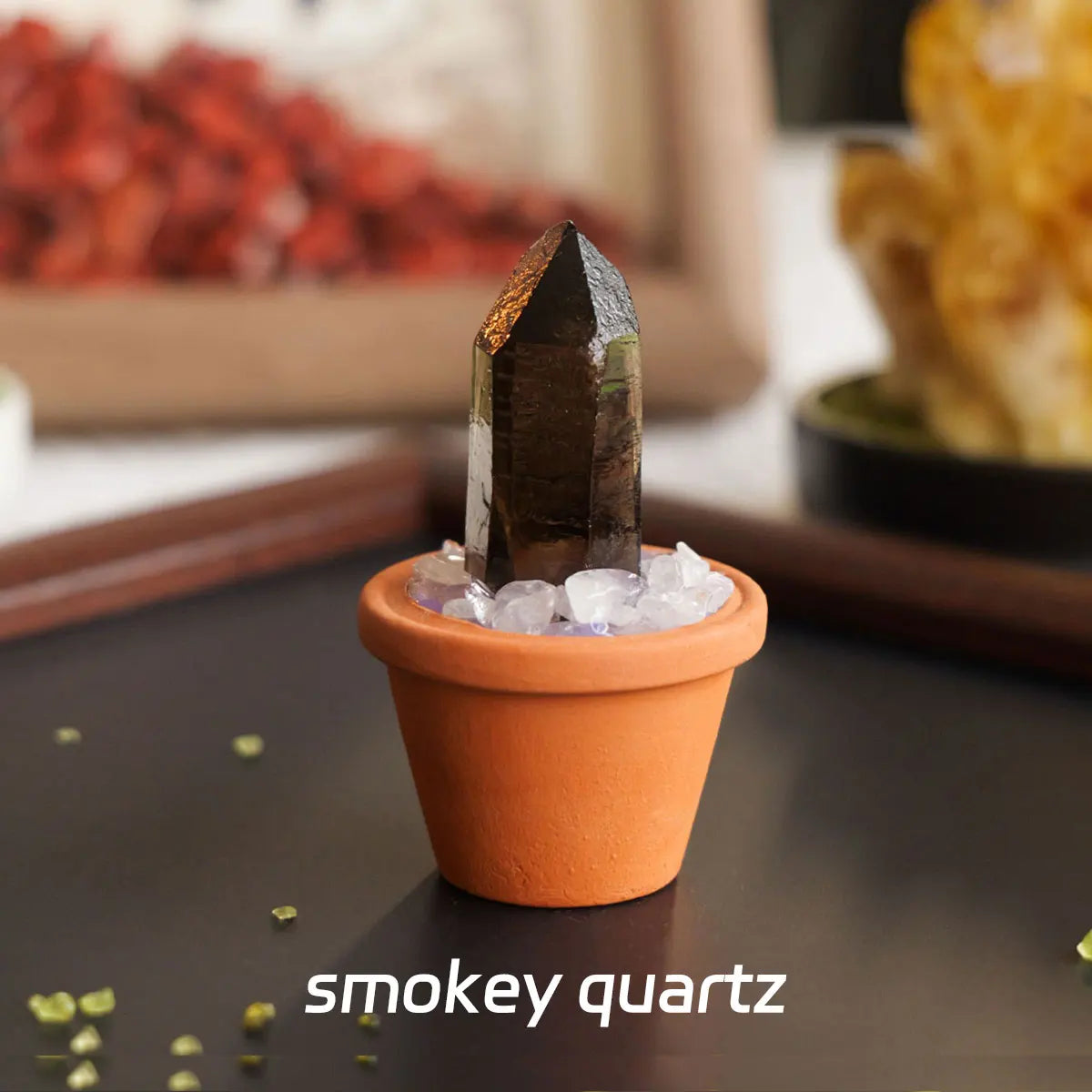 A dark smoky quartz point crystal sits in an orange pot filled with clear ice on a dark surface.