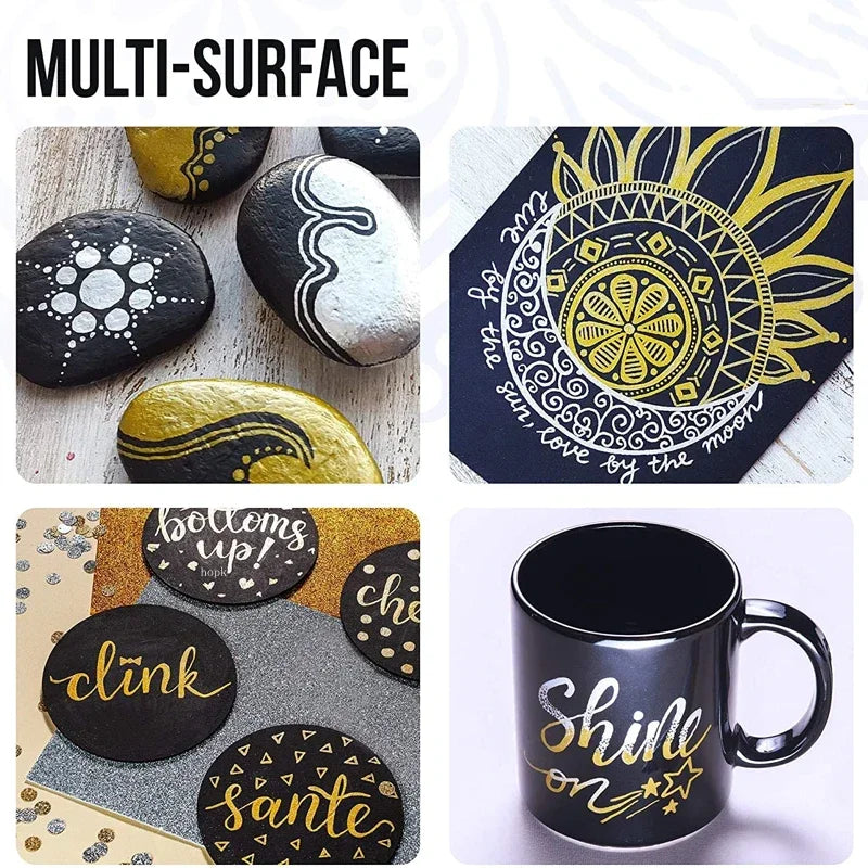 A collection of multi-surface art featuring black and gold paint pens on various surfaces like stones, paper, and a mug.