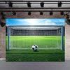 A soccer goal net and a soccer ball on a green field set against a brick wall backdrop.